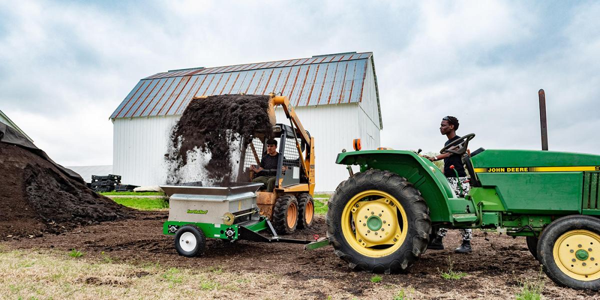 Student workers use a compost spreader at Terp Farm